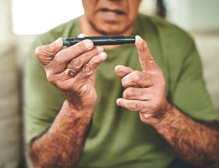 Older man using a lancing device to prick finger for blood glucose test.