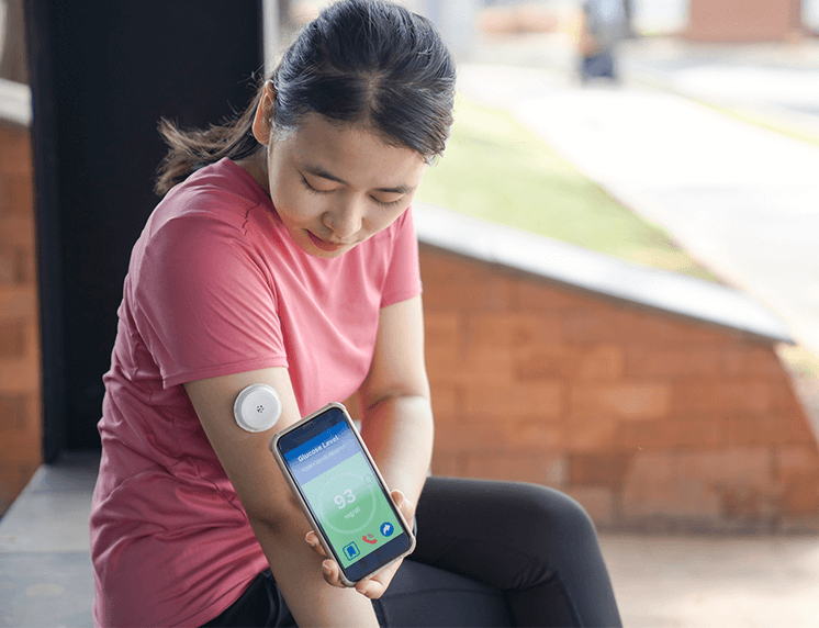 Young woman in athletic clothing checking her blood glucose using her continuous glucose monitor sensor and smartphone.