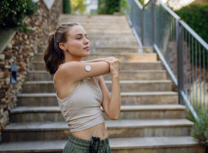Young, active woman wearing a continuous glucose monitor stretching her arms out before a run.